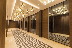 A modern hotel corridor with geometric patterned flooring, reflective surfaces, and contemporary lighting fixtures.