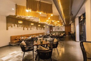 A spacious dining area with high ceilings, hanging golden chandeliers, and modern furniture.