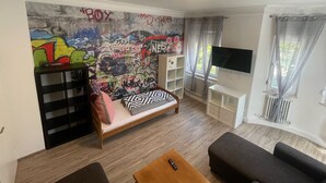 Une pièce avec un mur couvert de graffitis, un lit, une télévision et une fenêtre avec des rideaux.