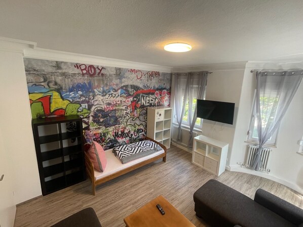 A room with a graffiti-covered wall, a bed, a TV, and a window with curtains. - Alpen-Hostel Mittelstation Nord, Buxacher Straße 23, with bike rentals (Memmingen)