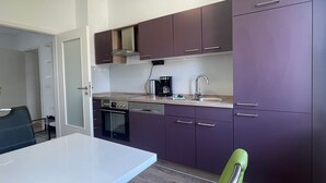 Une cuisine de taille réduite avec un plan de travail blanc, des appareils en acier inoxydable et des meubles de couleur violette.