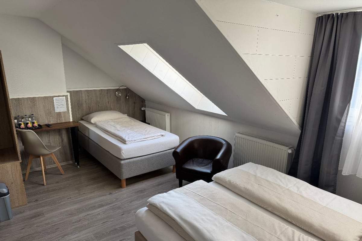 Habitación de hotel compacta con cama de altillo, un escritorio con silla y tragaluz.