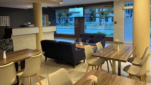 Un moderno vestíbulo de hotel con un mostrador de recepción de madera, un sofá negro y un área de comedor con una mesa y sillas de madera.
