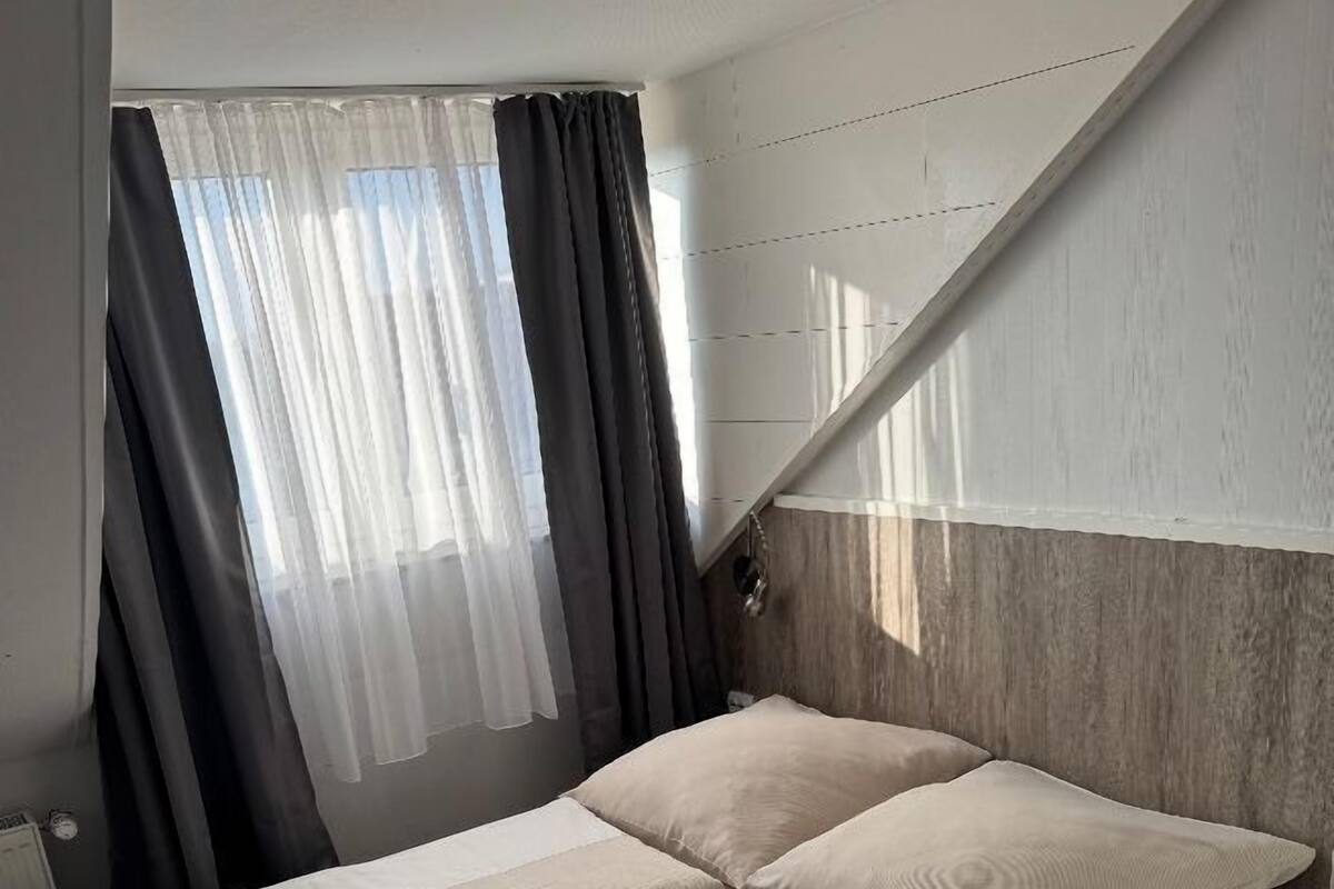 Un dormitorio moderno con cama, cortinas y techo inclinado.