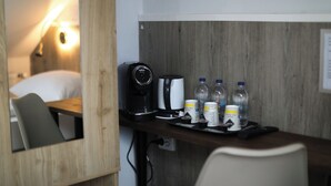 Habitación de hotel con escritorio de madera, cafetera, agua embotellada y una bandeja con control remoto.