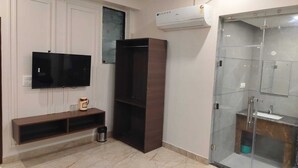 Une salle de bain moderne avec une douche à parois de verre, un climatiseur fixé au mur et un téléviseur posé sur une étagère en bois.
