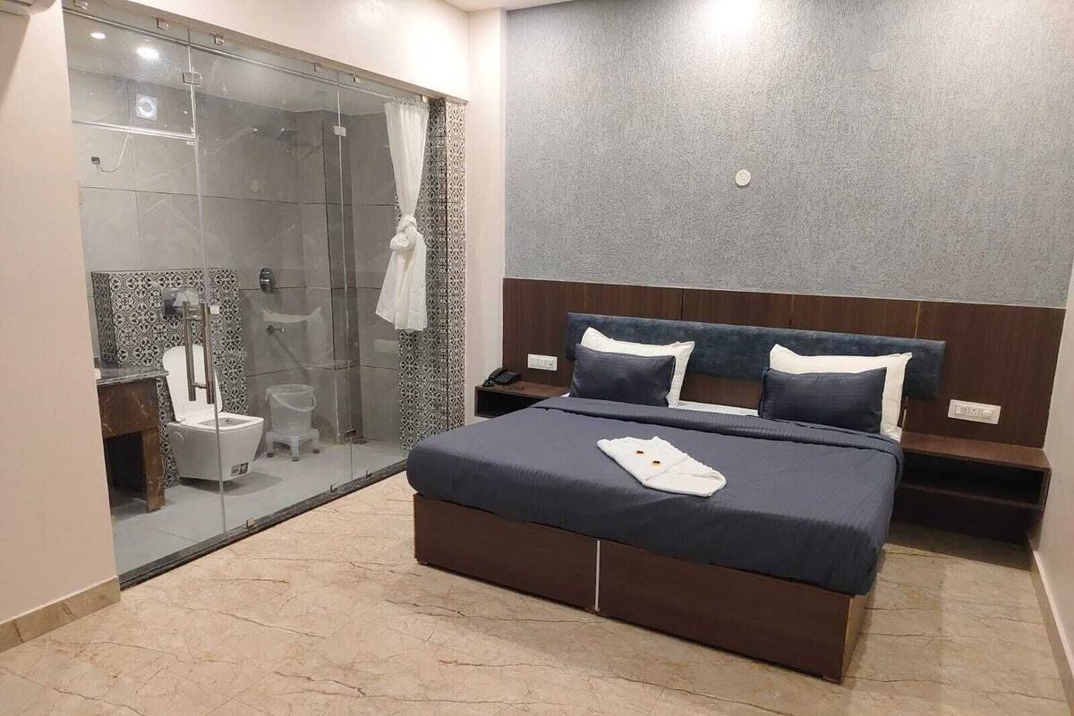 Una habitación de hotel moderna con una cama grande, cabina de ducha de vidrio y una mesita de noche pequeña.