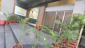 L’entrée d’un hôtel, avec une enseigne indiquant « HÔTEL JOY » et une variété de plantes en pot devant.