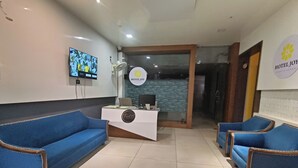 Un espace d’accueil d’hôtel comprenant un comptoir de réception, deux canapés bleus, un téléviseur fixé au mur et un logo sur le mur.