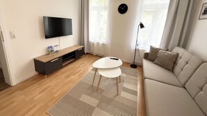 Una sala de estar moderna con un televisor de pantalla plana, una mesa redonda de centro, un sofá y una lámpara de pie.