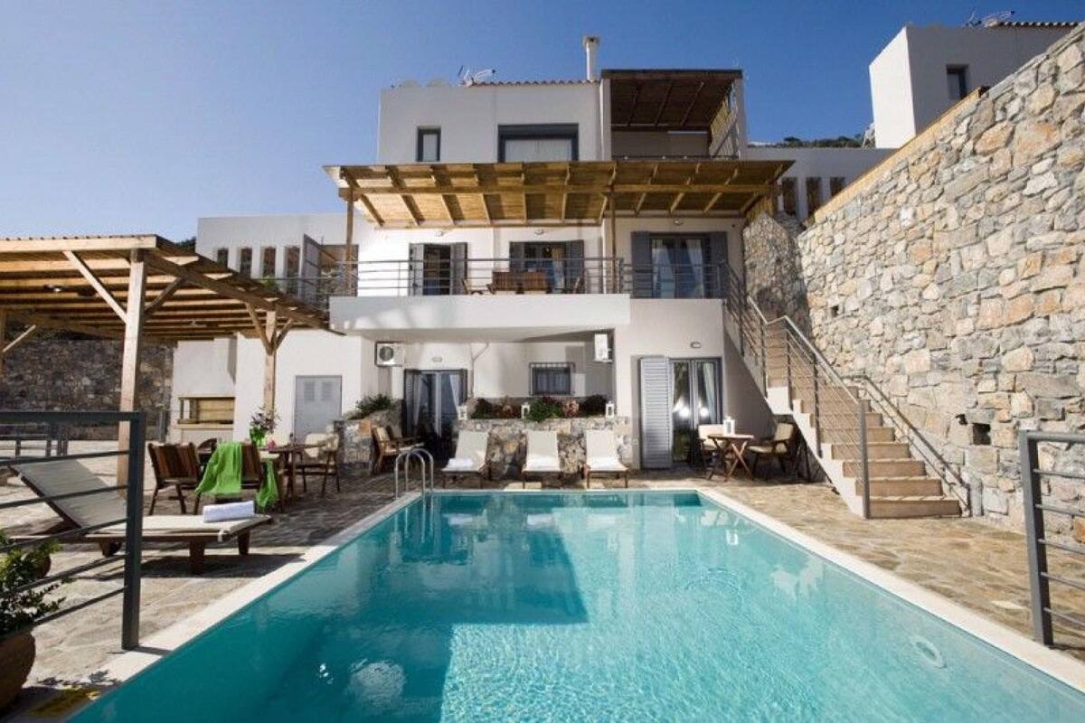 A modern two-story building with a pool, outdoor seating, and a stone wall.