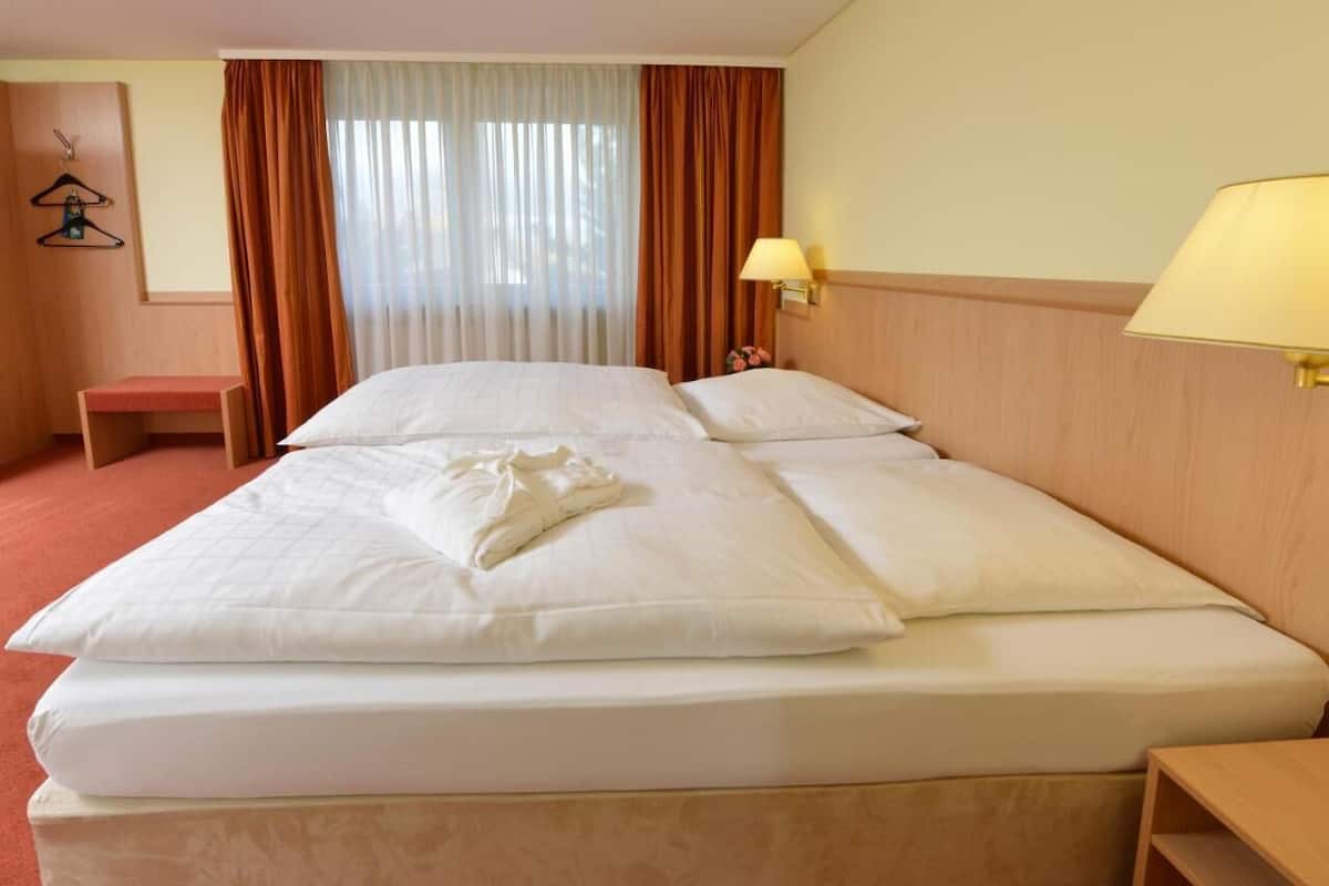 A hotel room with a large bed, a bedside table, a lamp, a chair, and a window with curtains.
