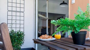 Una mesa de madera con una planta en maceta, un plato con croissants y un vaso de jugo de naranja en un patio.