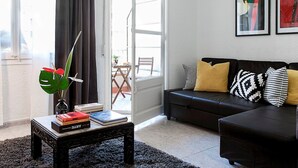 Una sala de estar moderna con un sofá negro, una mesa de centro con libros, una planta y vistas al exterior.
