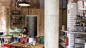 Interior rústico de un café con paredes de ladrillo visto, mobiliario de madera y diferentes opciones de asientos.
