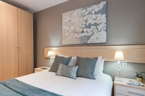 Quarto de hotel com cama, duas luminárias de cabeceira, mesa de cabeceira, armário e um quadro na parede.