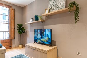 Una habitación con una televisión sobre un mueble de madera, una planta en maceta y una ventana con puerta de madera.