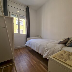 A bedroom with a bed, a bedside table, a window with curtains, and a view of a yellow building. - Walk to Camp NOU - Wi-fi AC 3 Bed by Myrentalhost (L'Hospitalet de Llobregat)