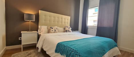 A bedroom with a bed, a nightstand, a lamp, and a view of the outside.