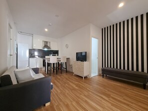 A modern living room with a sofa, a TV, and a dining area with chairs and a table.