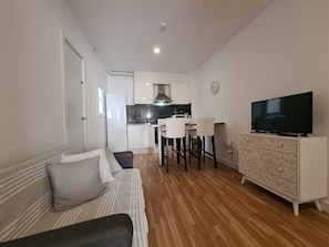 A compact living space with a kitchenette, a sofa, a television, and a patterned cabinet.