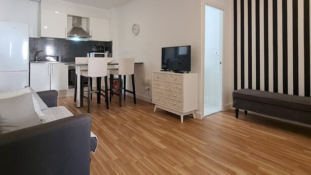 A modern living room with a sofa, a TV, and a dining area with a table and chairs. - Walk to Camp NOU - Wi-fi AC 3 Bed by Myrentalhost (L'Hospitalet de Llobregat)