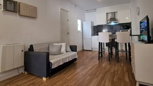 A modern living room with a sofa, a dining area with chairs, a kitchen with a stove, and a TV. - Walk to Camp NOU - Wi-fi AC 3 Bed by Myrentalhost (L'Hospitalet de Llobregat)