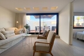 A modern living room with a sofa, armchair, and a small table. There is a sliding glass door leading to an outdoor area with a table and chairs. - Modern Penthouse With Views Near Paseo De Gracia By Myrentalhost (Barcelona)