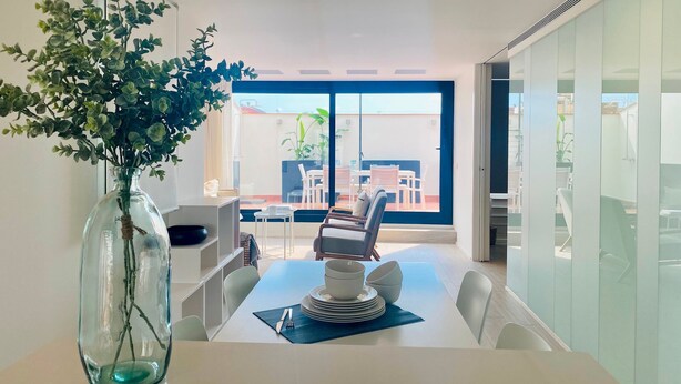 A modern dining area with a glass table, white chairs, and a vase with green foliage. - Modern Penthouse With Views Near Paseo De Gracia By Myrentalhost (Barcelona)