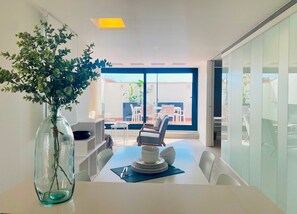 A modern dining area with a glass table, white chairs, and a vase with green foliage. - Modern Penthouse With Views Near Paseo De Gracia By Myrentalhost (Barcelona)