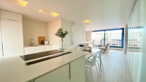 A modern kitchen with white cabinetry, a central island, and a dining area with white chairs. - Modern Penthouse With Views Near Paseo De Gracia By Myrentalhost (Barcelona)