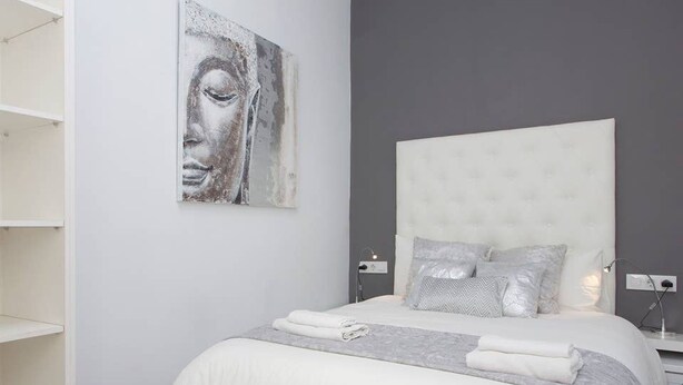 Une chambre à coucher avec un grand lit, une tête de lit grise et une œuvre d’art accrochée au mur.