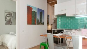 Une cuisine moderne avec des meubles blancs, un pare-feu vert et un coin repas comprenant une table en bois et des chaises en métal.