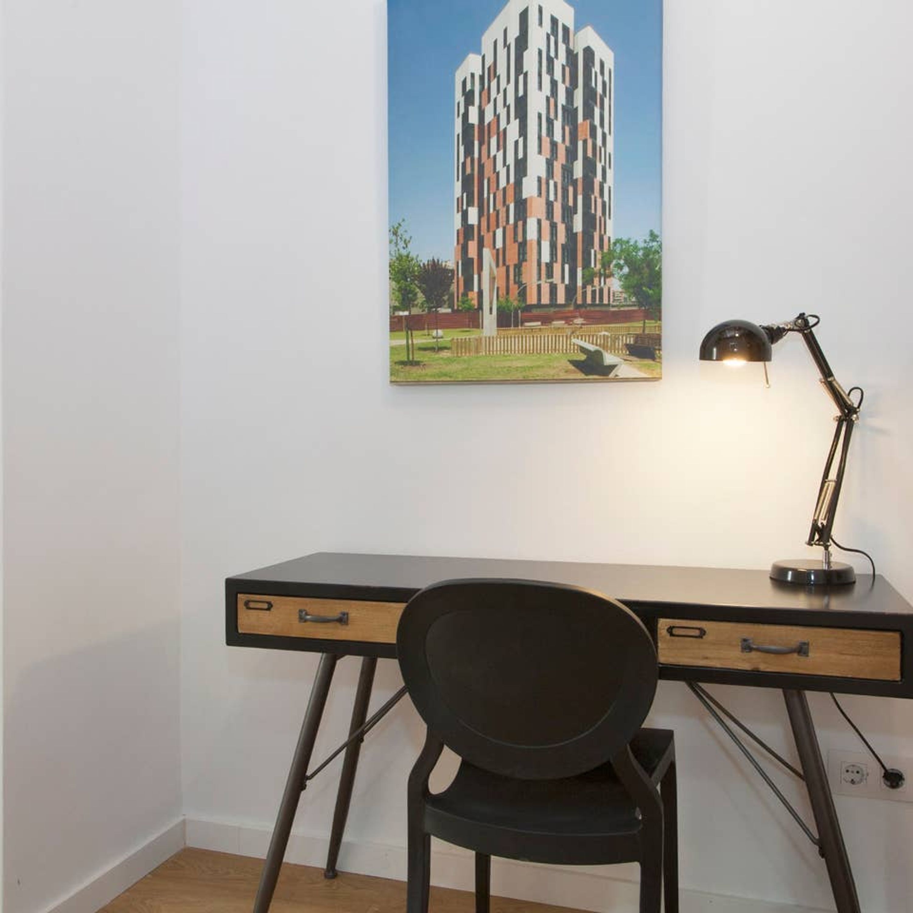 A modern desk with a chair, a desk lamp, and a framed architectural drawing on the wall.
