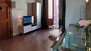A room with wooden beams on the ceiling, a television on a stand, a glass table, and a vase with flowers. - Catalan Comfort Near Sagrada Familia (Barcelona)