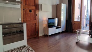 A modern kitchen with a stove, oven, and a wooden door. There is a TV on a stand and a small table with a lamp. - Catalan Comfort Near Sagrada Familia (Barcelona)