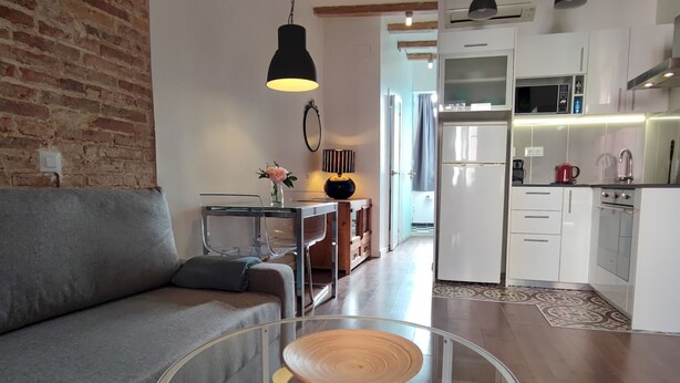 A modern living room with a grey sofa, a glass coffee table, and a kitchen in the background. - Catalan Comfort Near Sagrada Familia (Barcelona)