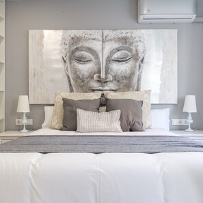 Une chambre avec un grand lit, deux tables de chevet, un climatiseur fixé au mur et une grande œuvre d’art au-dessus du lit.