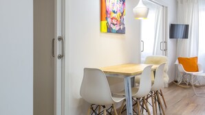 Ein moderner Essbereich mit einem Holztisch, weißen Stühlen und einem farbenfrohen Gemälde an der Wand.