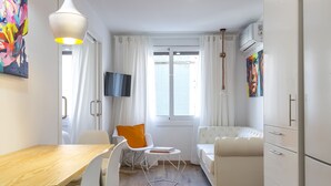 Eine moderne Küche mit Holztisch, weißen Stühlen, einer Couch und einem an der Wand montierten Fernseher.