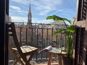 A balcony with a wrought iron railing, a wooden chair, a potted plant, and a magazine on a small table. - Luminous Designer Loft Style Apt Eixample Views By Myrentalhost (Barcelona)