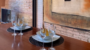 A dining area with a brick wall, a large abstract painting, and a modern table setup with glasses and plates. - Luminous Designer Loft Style Apt Eixample Views By Myrentalhost (Barcelona)