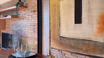 Comedor con pared de ladrillo, un cuadro abstracto grande y una mesa moderna con vasos y platos.