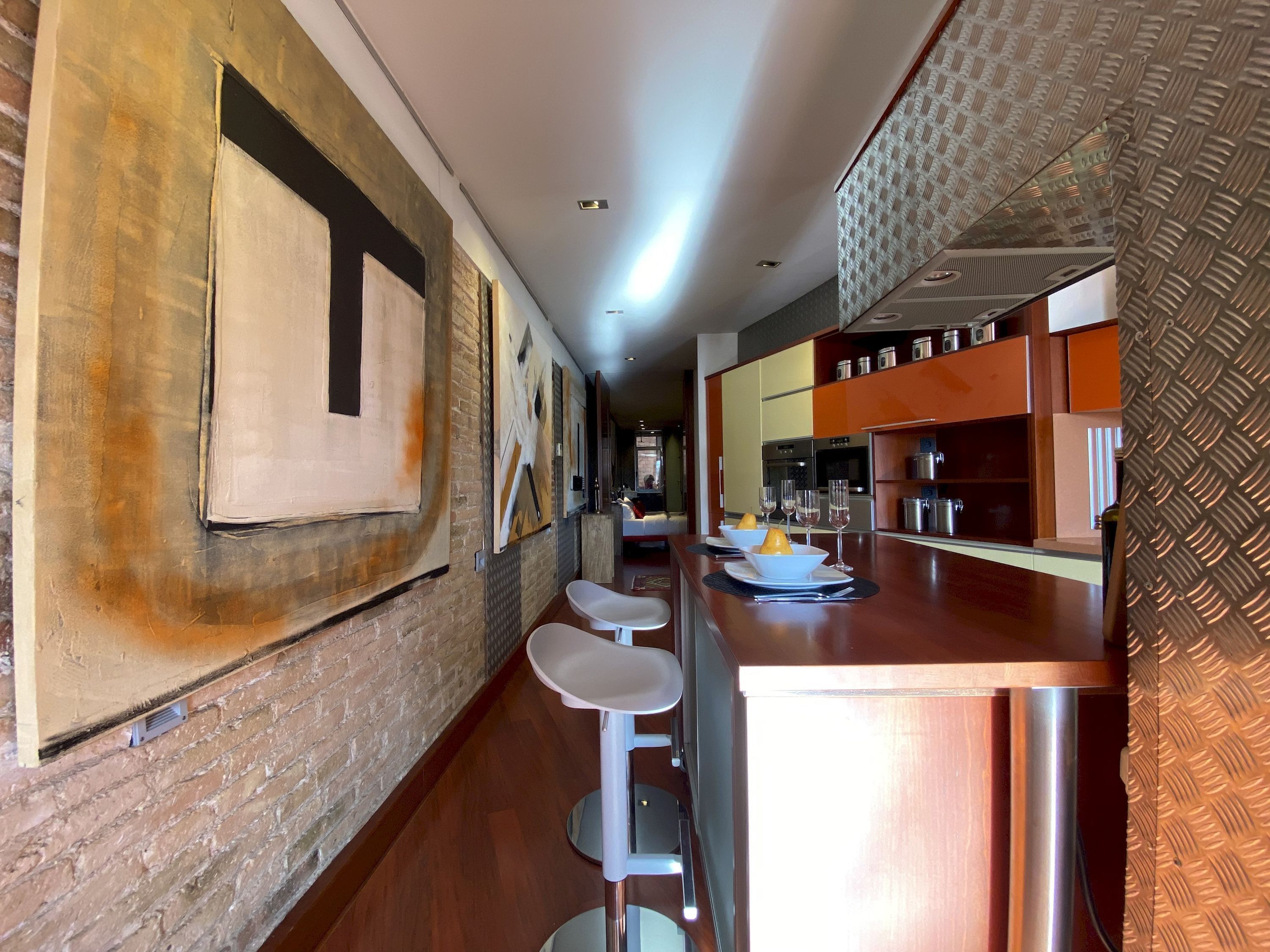 A modern kitchen with a bar area, stainless steel appliances, and a brick wall with abstract art.