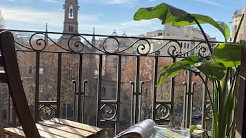 Un balcón con vistas a la aguja de una iglesia, una planta en maceta y un periódico sobre una mesa.