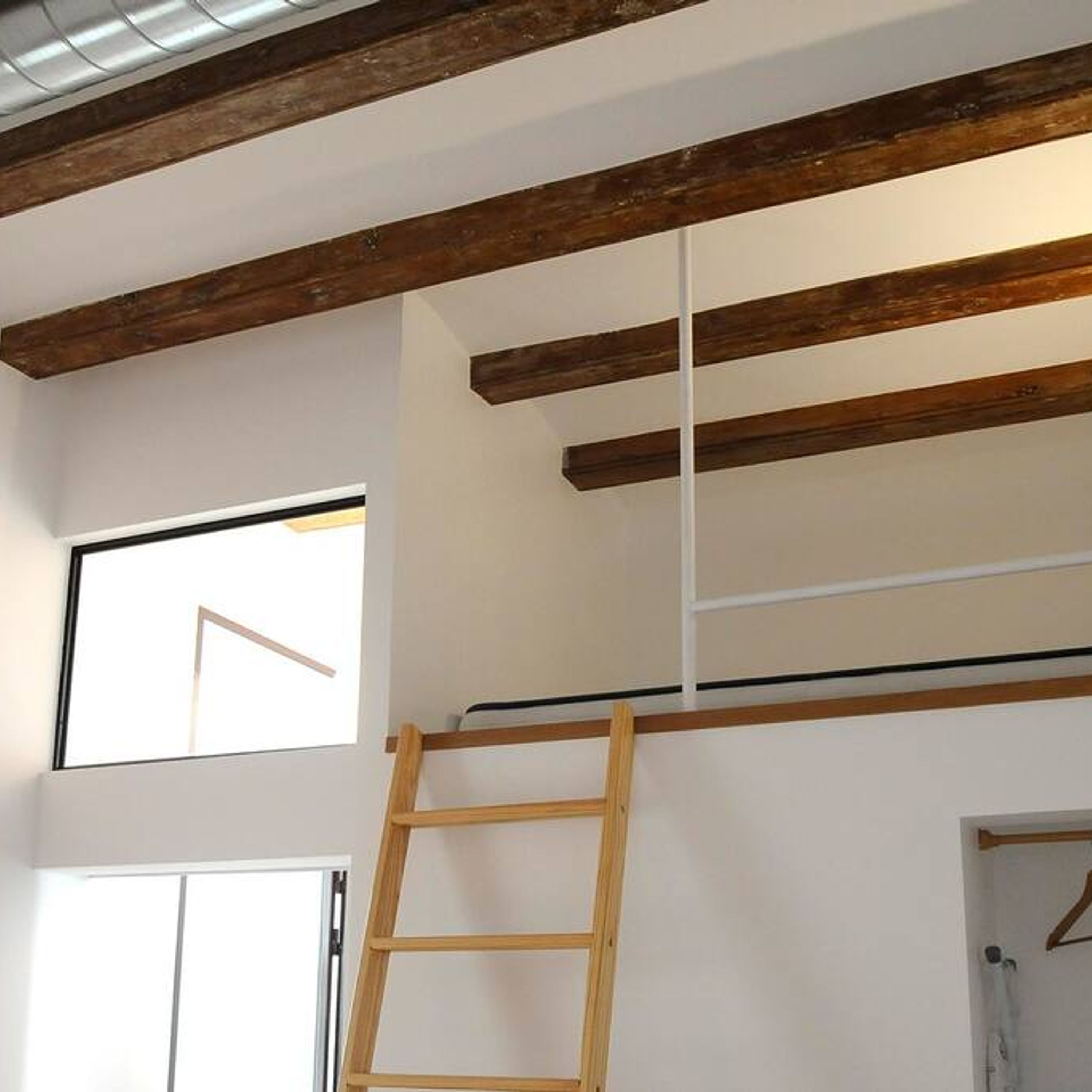 A room with exposed wooden beams, a window, a door, and a ladder.