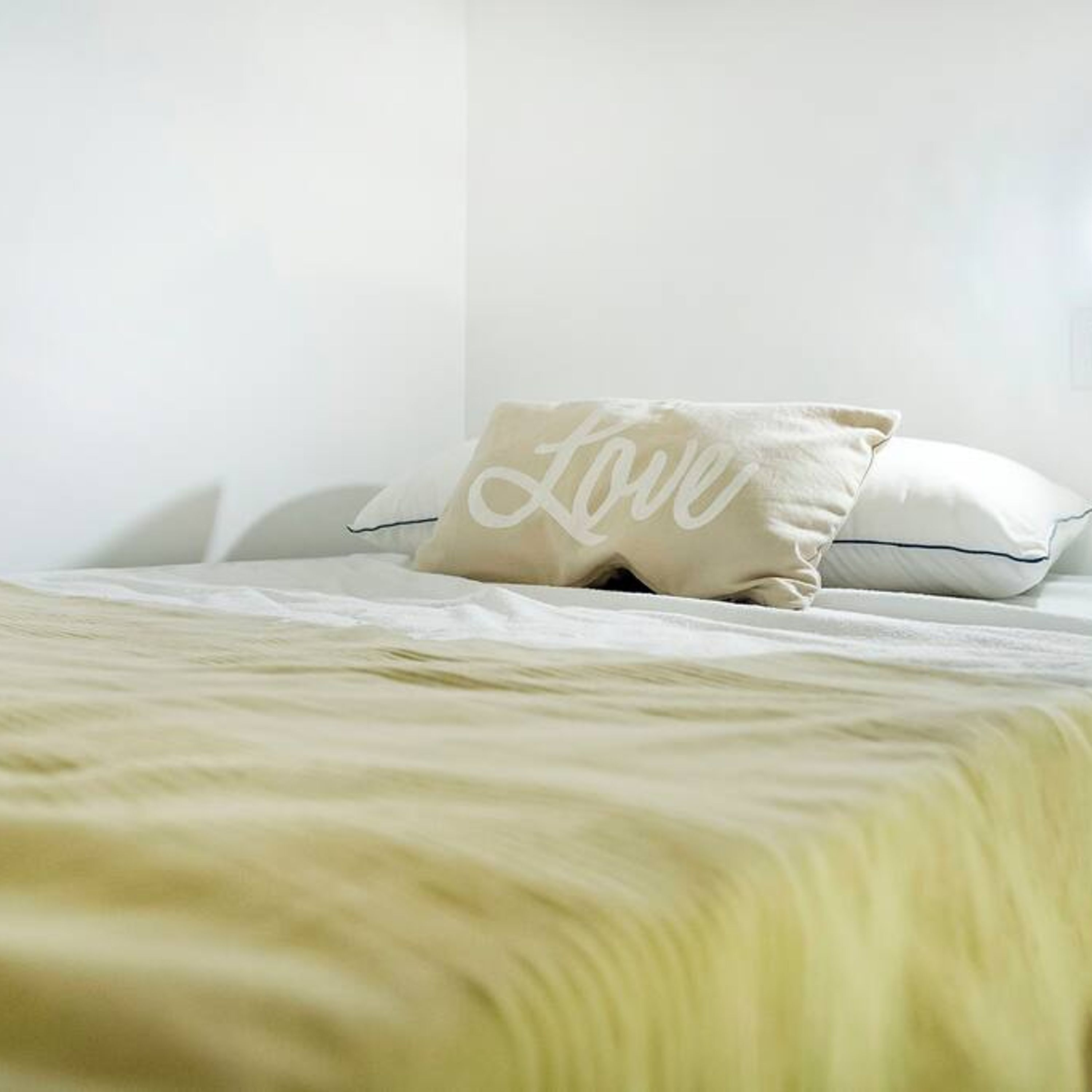 Una cama con un almohadón blanco y un almohadón con la palabra 'Love'.