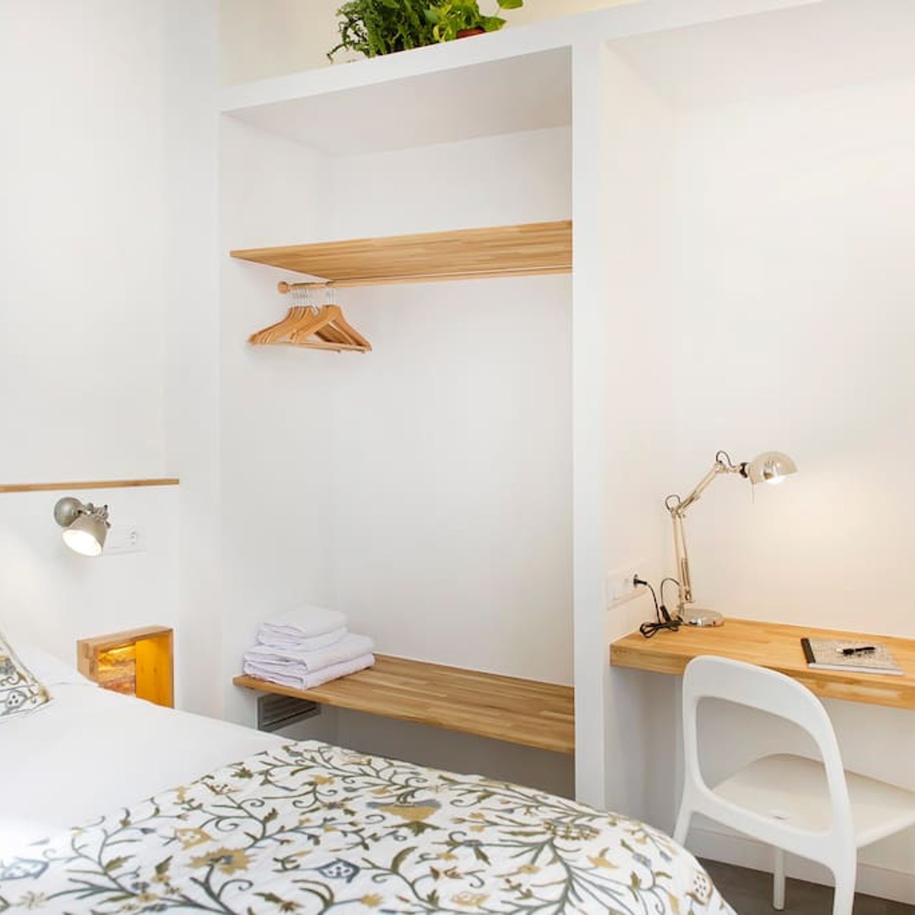 A modern bedroom with a wooden bed, a desk with a lamp, and a hanging plant.