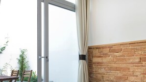 A hotel room with a bed, a wooden headboard, a brick wall, a sliding glass door, and a table with chairs outside. - Unique Architects Apartment IN Trendy Central Poble SEC By Myrentalhost (Barcelona)