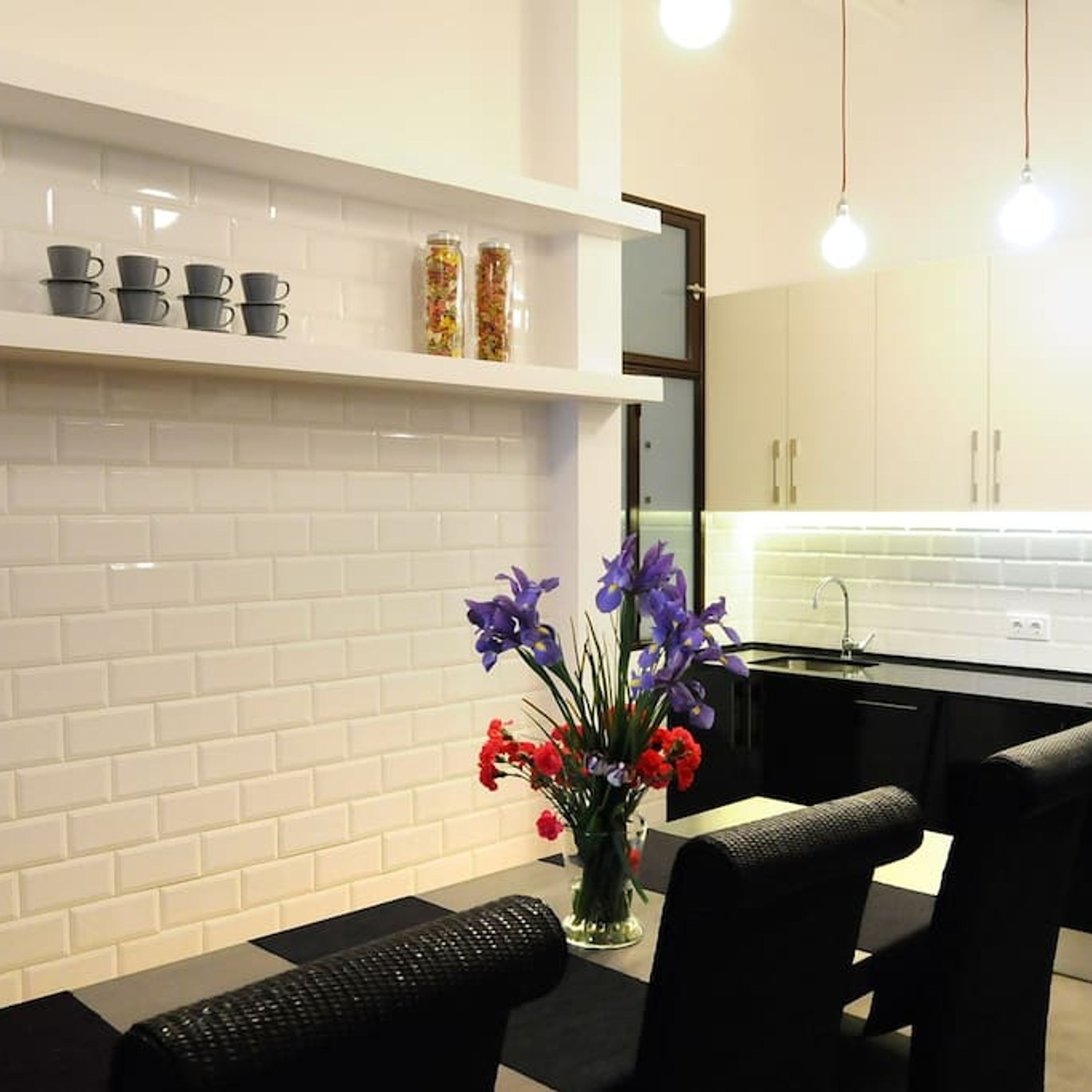 A modern kitchen with white subway tiles, a black countertop, and a dining area with a black chair and a vase of flowers.
